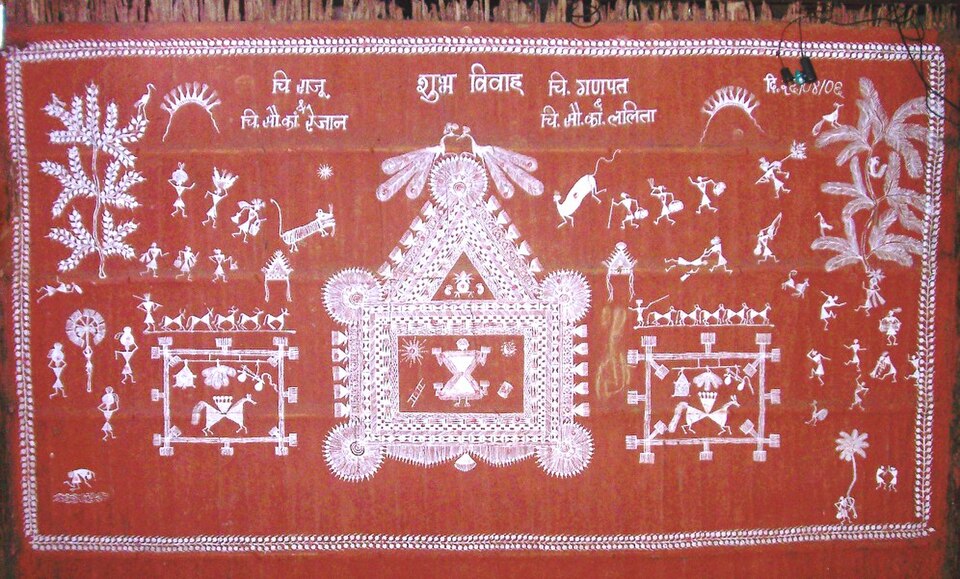 A Warli wedding chauk painted in white rice paste on a red-ochre mud wall: a large square ritual enclosure at the centre flanked by two smaller framed panels with horses, surrounded by rows of matchstick figures dancing, drumming and carrying pots, with trees, birds and animals filling the border, headed by the Devanagari words 'शुभ विवाह'