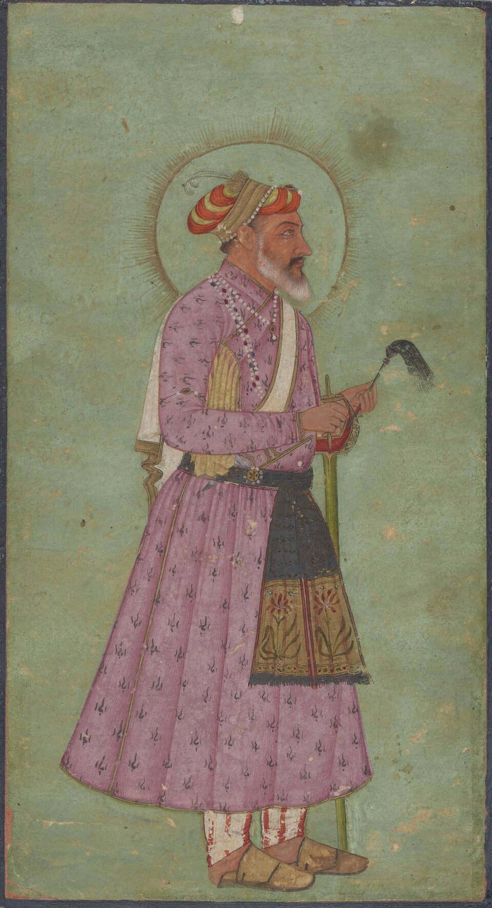Mughal album miniature of Aurangzeb standing in profile against a pale green ground: a white-bearded emperor with a golden halo behind his head, in a pink flowered jama with pearl strings and a patka, holding a sword hilt and a black falconry lure