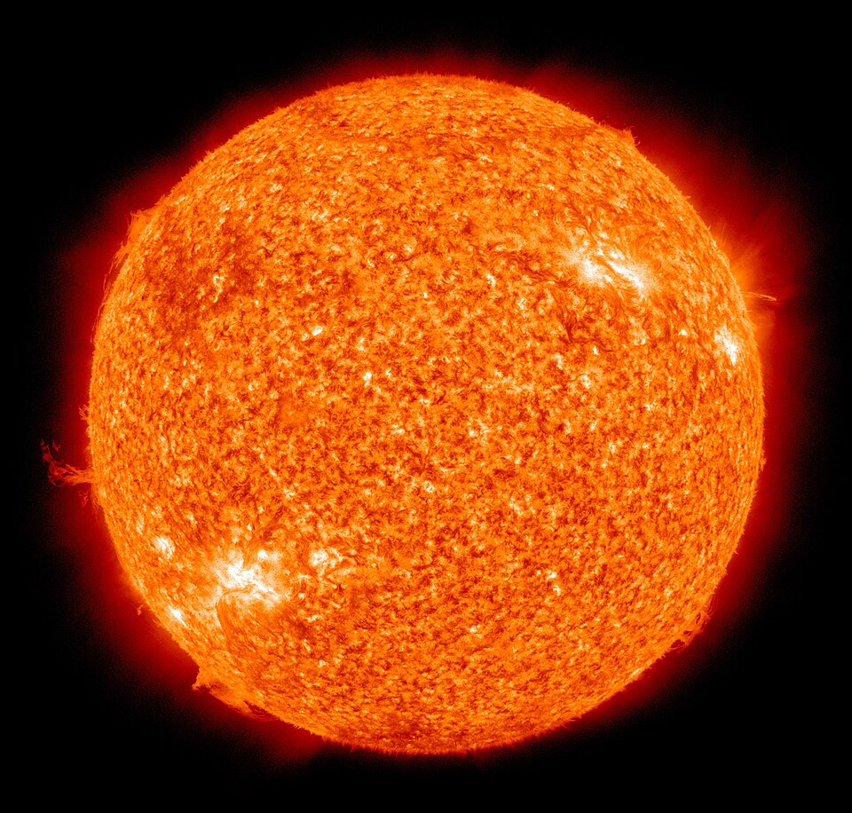 The full disc of the Sun in ultraviolet false colour against black space — a mottled orange surface of granular plasma with bright white active regions near the limb and a dark prominence arching off the left edge