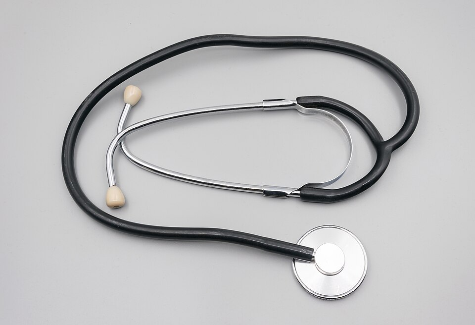 A binaural stethoscope laid flat: a flat metal chest-piece with a diaphragm, black rubber tubing and a metal binaural headset with two earpieces
