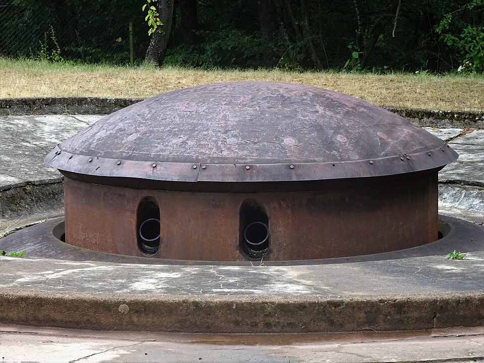 A rusted retractable armoured gun turret of the Maginot Line raised out of its concrete block at Ouvrage du Hackenberg, its domed steel cupola showing two gun embrasures