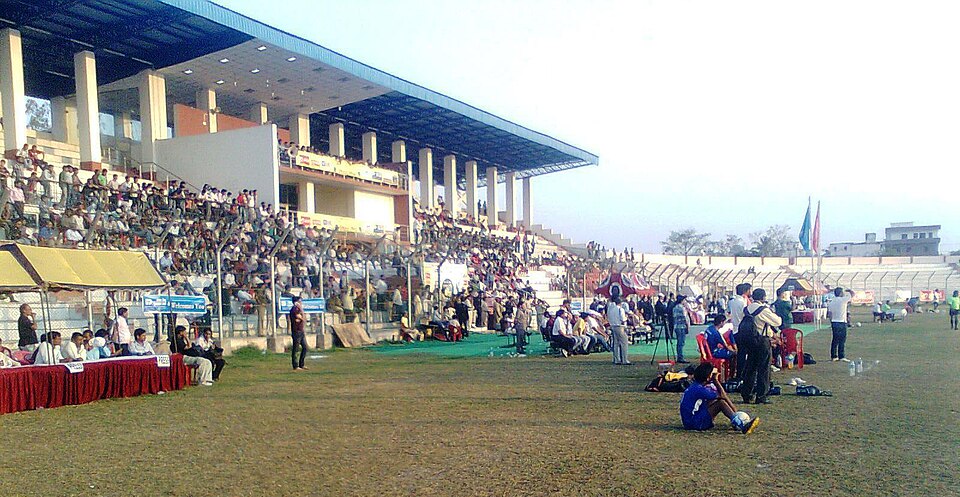 The covered spectator pavilion and grass playing field of the Pataliputra Sports Complex at Kankarbagh, Patna, with crowds filling the stands during an event