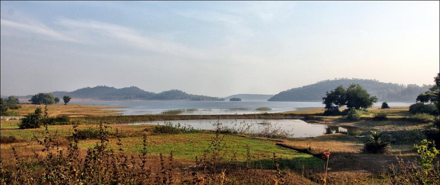 Forested Himalayan foothill ridges at Valmikinagar in West Champaran, Bihar, rising beyond a wide sheet of water and a belt of grassland and scrub