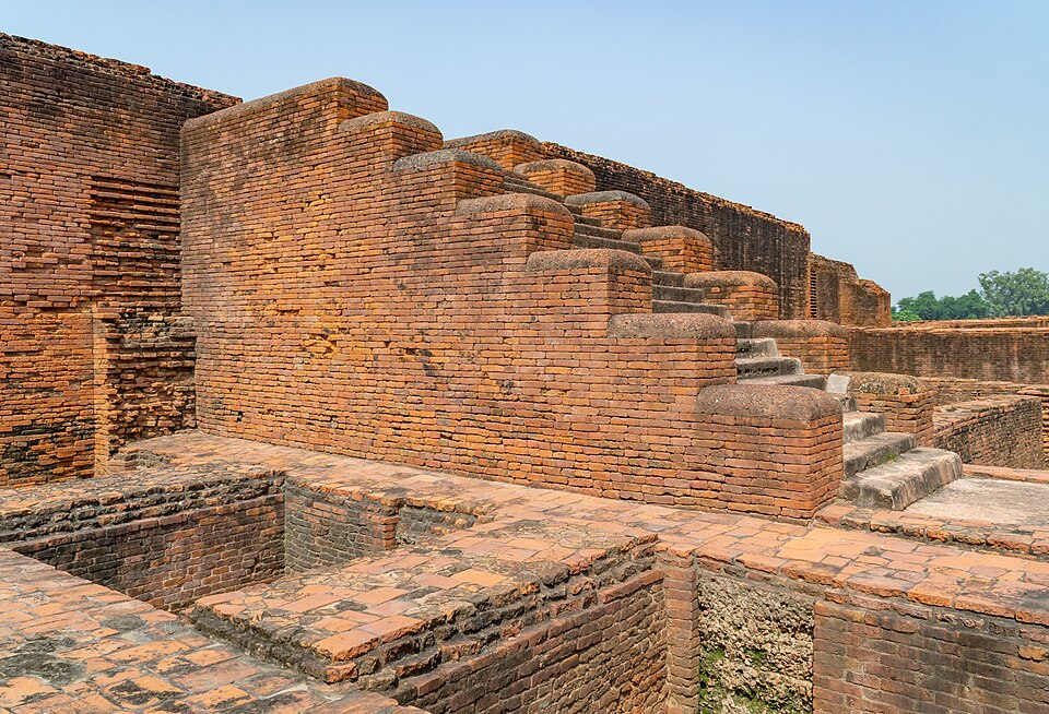 Excavated red-brick monastery ruins at Nalanda, a long wall of rounded brick buttresses stepping away into the distance above the exposed foundations of monks' cells