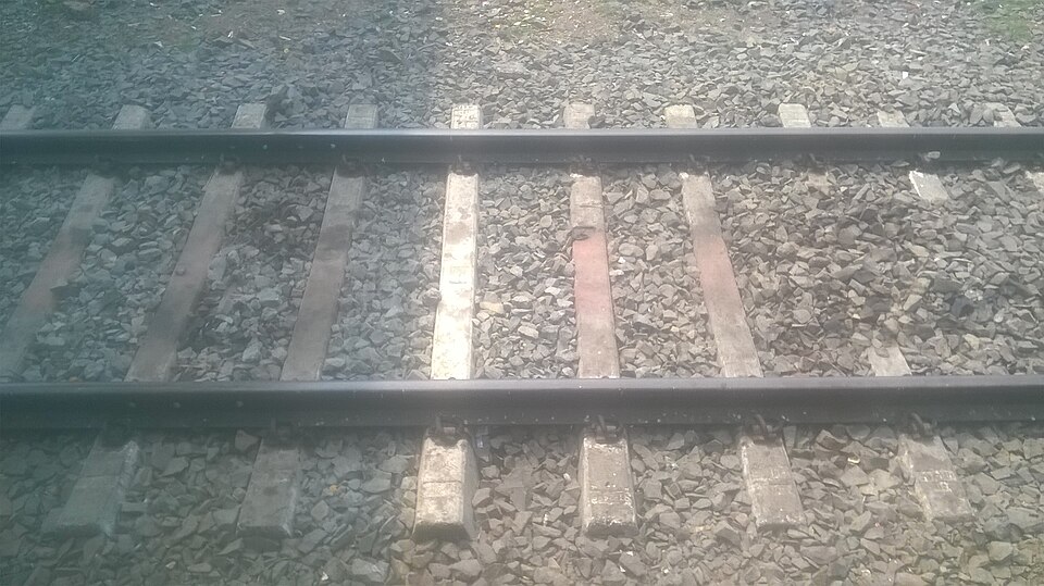 Close view of a pair of steel broad-gauge railway rails running away over concrete sleepers bedded in stone ballast
