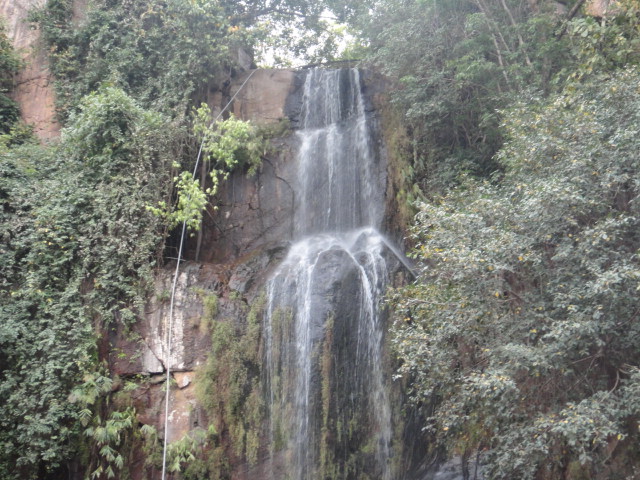 Kakolat waterfall in Nawada district, Bihar, a slender white stream dropping in two stages down a dark mossy rock face into the pool below, framed by dense green forest