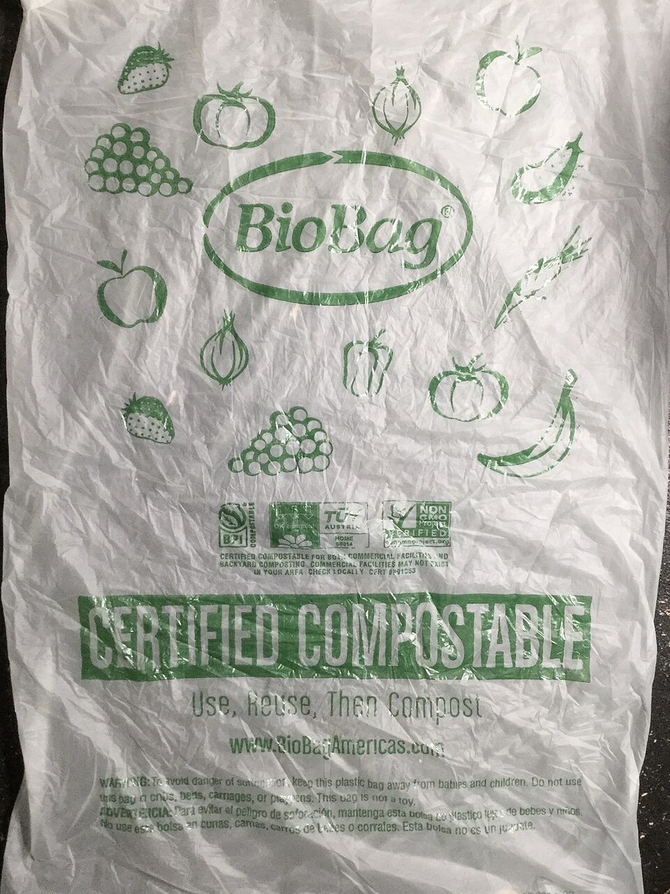 A thin white bioplastic bag printed in green with fruit and vegetable outlines, the words CERTIFIED COMPOSTABLE across the lower half and a row of compostability certification logos above them