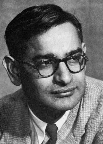 Black-and-white studio portrait of Har Gobind Khorana in a tweed jacket and tie, wearing heavy dark-rimmed round spectacles