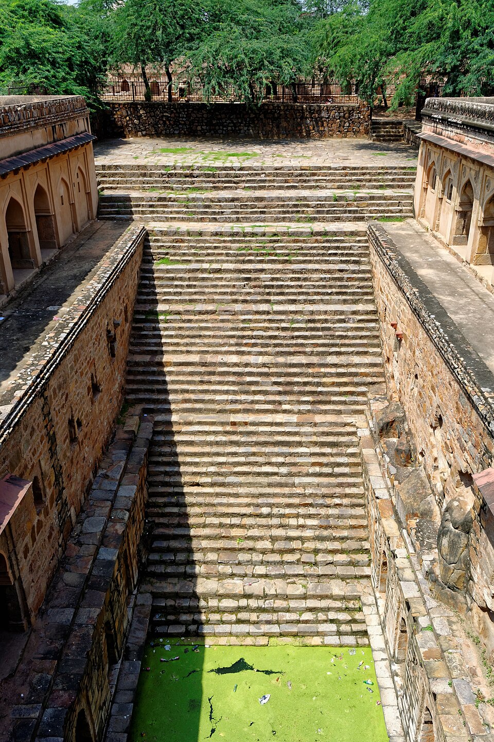 Rajon ki Baoli in Mehrauli Archaeological Park, Delhi: a wide flight of stone steps descending between arched colonnaded galleries to a green algae-covered water tank