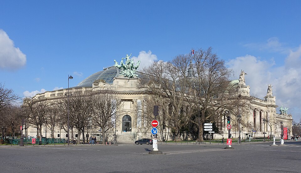 Exterior of the Grand Palais in Paris seen from Avenue Winston-Churchill, its Beaux-Arts stone facade topped by the glass-and-steel barrel vault and bronze quadriga sculptures