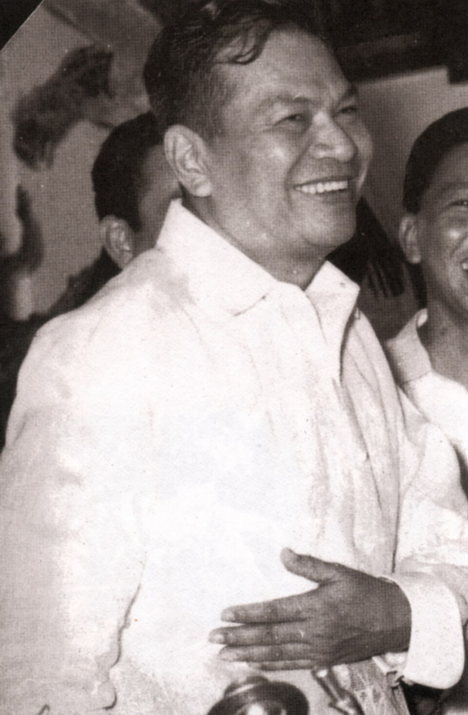 Black-and-white photograph of Ramon Magsaysay, seventh President of the Philippines, smiling in a white barong shirt among a crowd