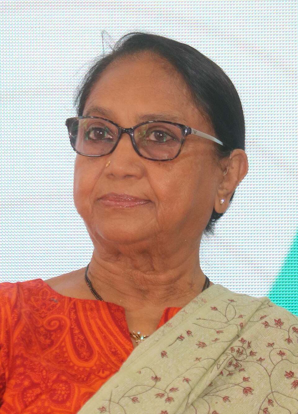 Portrait of the Kannada writer and lawyer Banu Mushtaq, wearing spectacles, an orange kurta and a pale embroidered sari drape