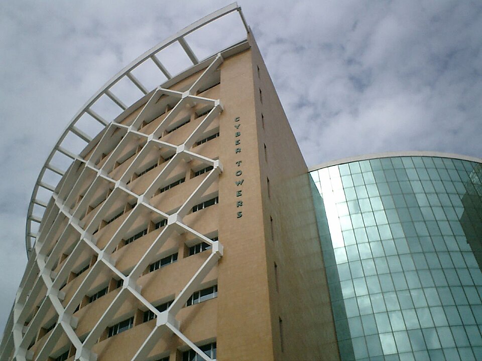 The Cyber Towers building in HITEC City, Hyderabad, seen from below: a curved lattice-braced facade carrying the vertical lettering CYBER TOWERS, with a green glass-clad wing alongside