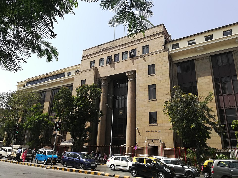 The stone-faced central office building of the Reserve Bank of India on Shahid Bhagat Singh Marg in Fort, Mumbai, its tall pilastered entrance bay carrying the RBI emblem above the doorway