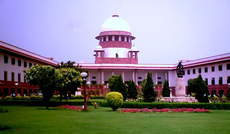 The Supreme Court of India on Tilak Marg, New Delhi, its central white dome rising above the red-and-white court block, seen across the front lawns