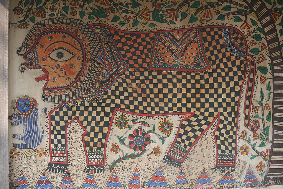 An authentic Madhubani wall painting in Bihar showing a large lion filled with black-and-ochre chequerboard pattern, a small blue human figure beside it and a hatched floral border