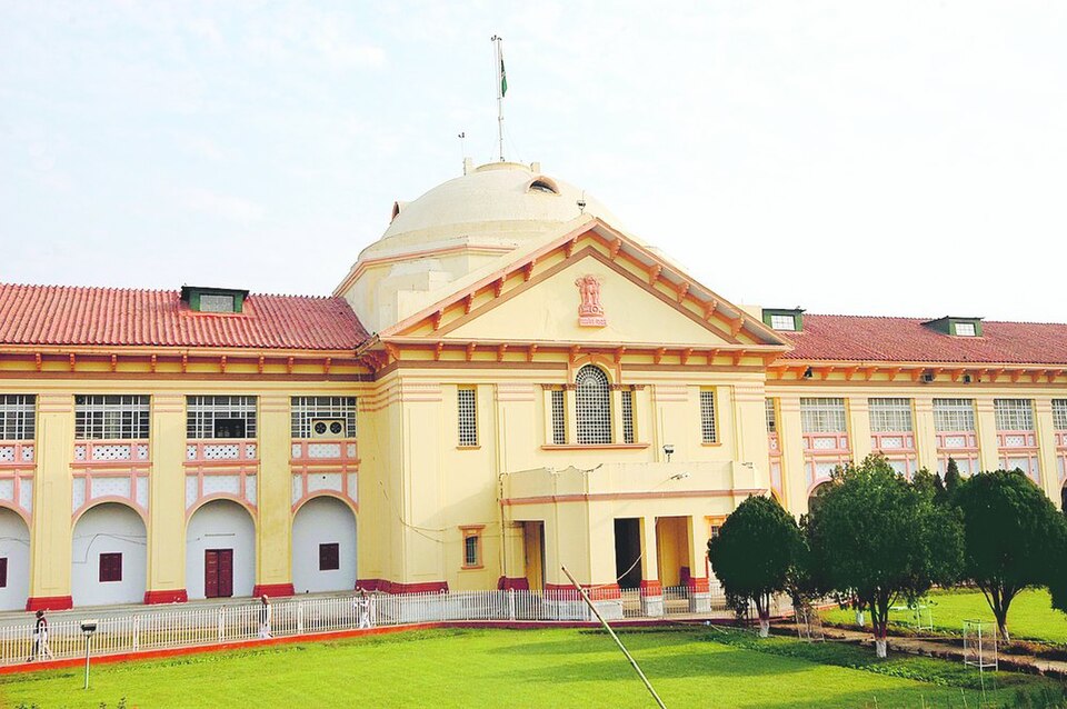 The Patna High Court building in Bihar: a long cream-and-red colonial block with a central pedimented portico carrying the State Emblem, a low dome above it and the national flag flying from the roof