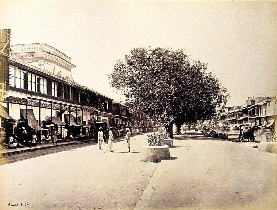 Samuel Bourne's 1860s photograph of Chandni Chowk, the principal street of Shahjahanabad in Old Delhi, showing the broad avenue with its central canal plinth, awninged shopfronts on either side and a large shade tree