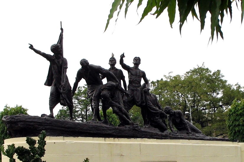 The Shaheed Smarak in Patna: a bronze group of seven young men surging forward over a rock, the foremost holding a flagstaff aloft, mounted on a plain stone plinth