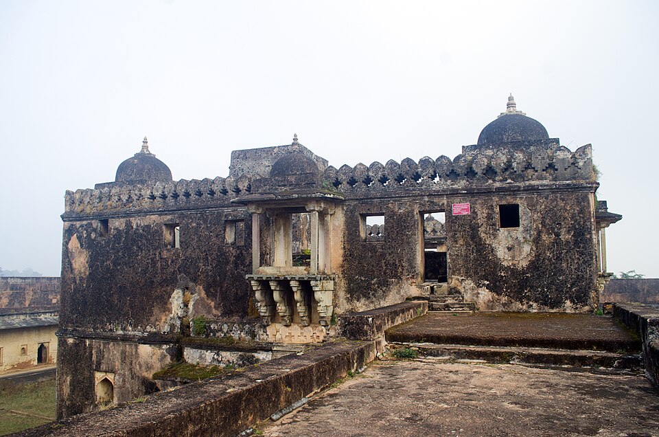 A ruined stone palace building inside Rohtasgarh Fort, with three weathered domes, a crenellated parapet and a bracketed balcony overlooking the fort's plateau