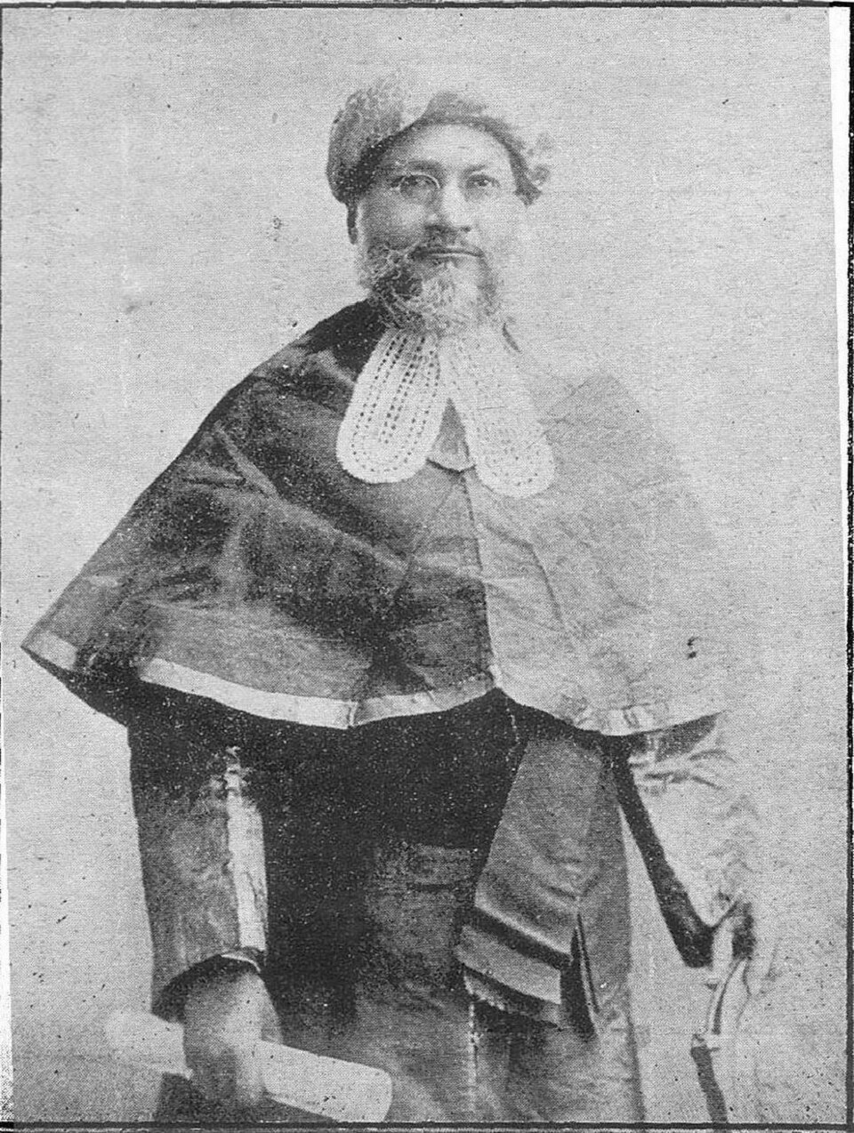 Sepia studio photograph of a bearded man in dark judicial robes with a wide white lace collar band and a soft rounded cap, standing three-quarter view and holding a rolled document.