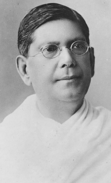 श्वेत-श्याम स्टूडियो चित्र, जिसमें अंडाकार तार-फ़्रेम के चश्मे पहने, दाढ़ी-मूँछ रहित अधेड़ व्यक्ति हैं; उनके काले बाल ऊँचे माथे से पीछे की ओर सँवारे हैं और एक कन्धे पर सफ़ेद दुशाला पड़ा है, पृष्ठभूमि सादी तथा हल्की है।