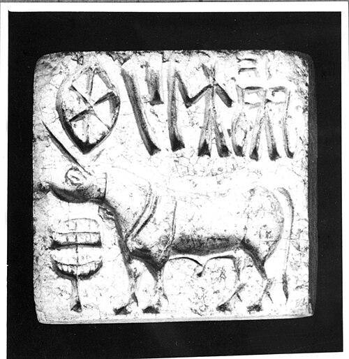 An archival photograph of a Harappan steatite seal carved with a bull-like animal standing below a row of Indus script signs