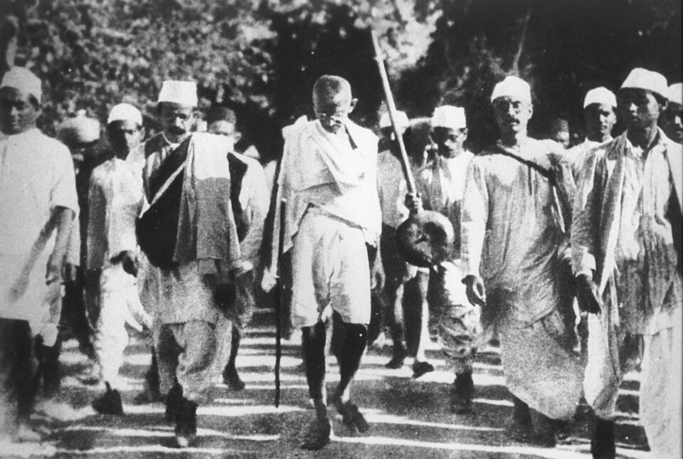 A 1930 photograph of Mahatma Gandhi walking with a staff at the head of a column of marchers during the Salt March