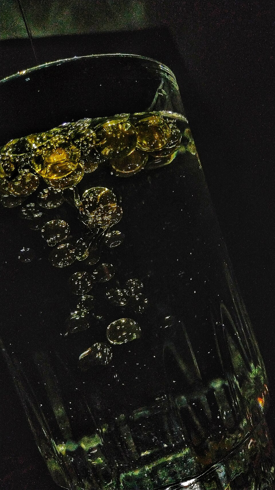 Golden oil droplets suspended in water inside a glass, coalescing into a separate layer at the surface instead of mixing