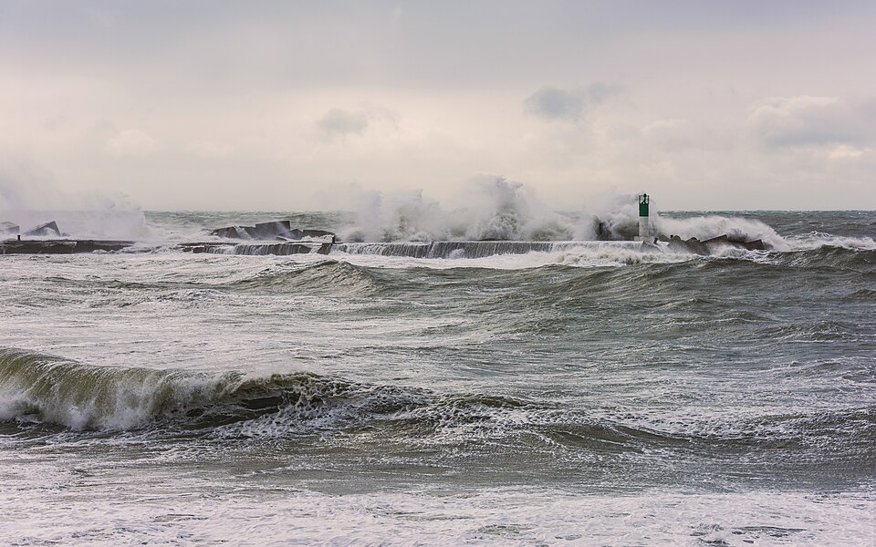 Successive parallel wave crests rolling in from the open sea towards a breakwater, with troughs between them