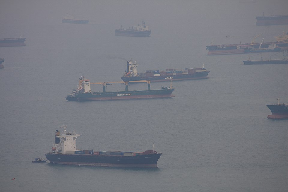 Cargo and container ships lying at anchor in the hazy waters of the Singapore anchorage