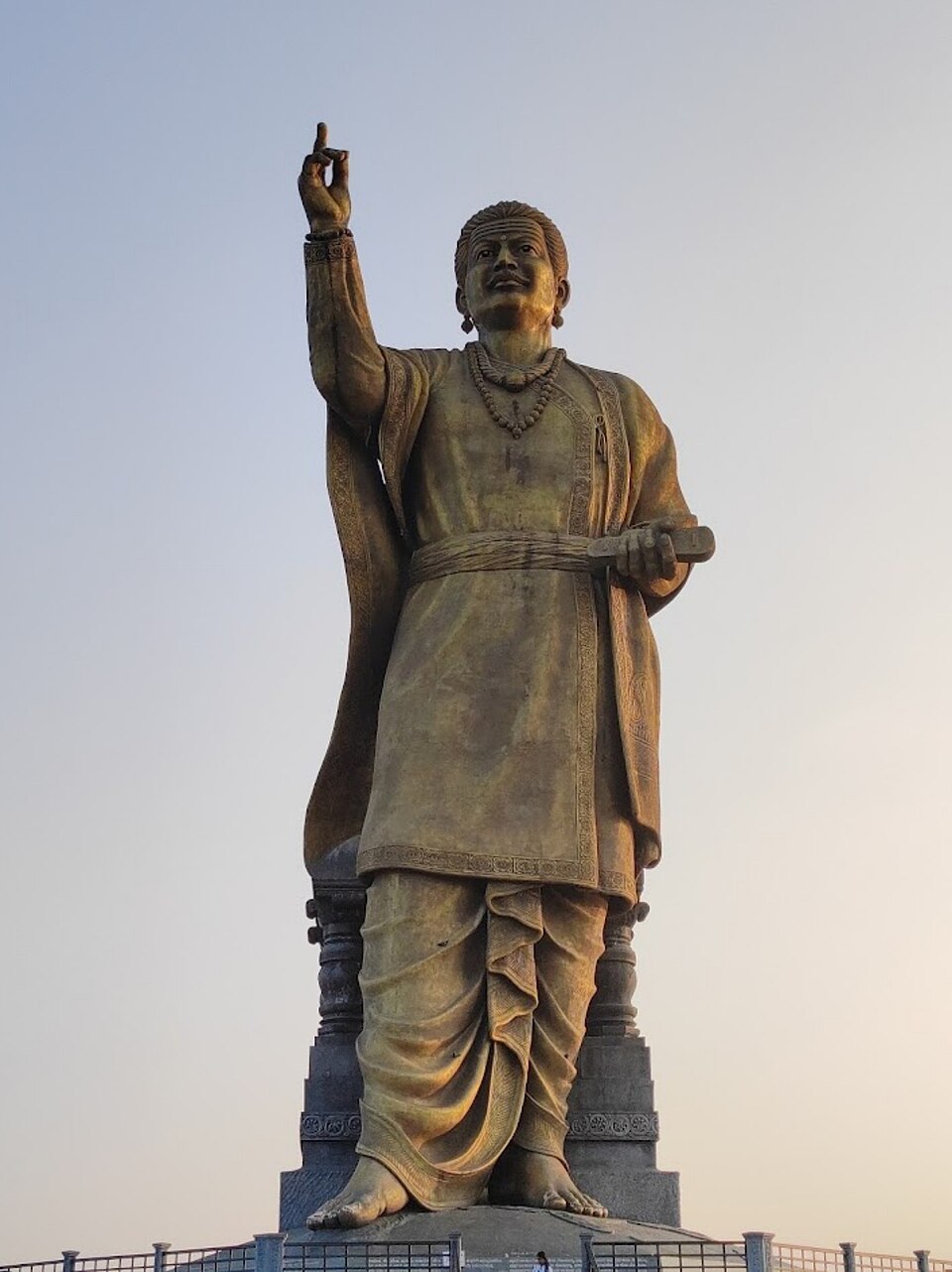 A tall bronze statue of the twelfth-century reformer Basavanna on a stone pedestal, one hand raised and a tablet held in the other