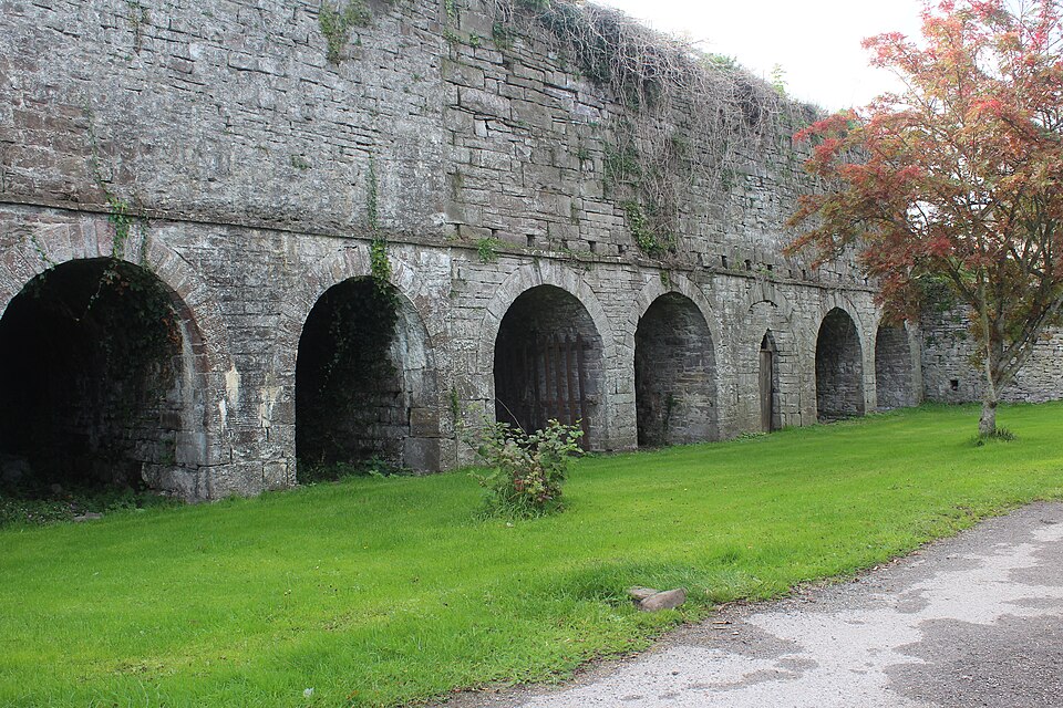 A bank of disused stone lime kilns built into a masonry retaining wall, with arched draw-holes at ground level