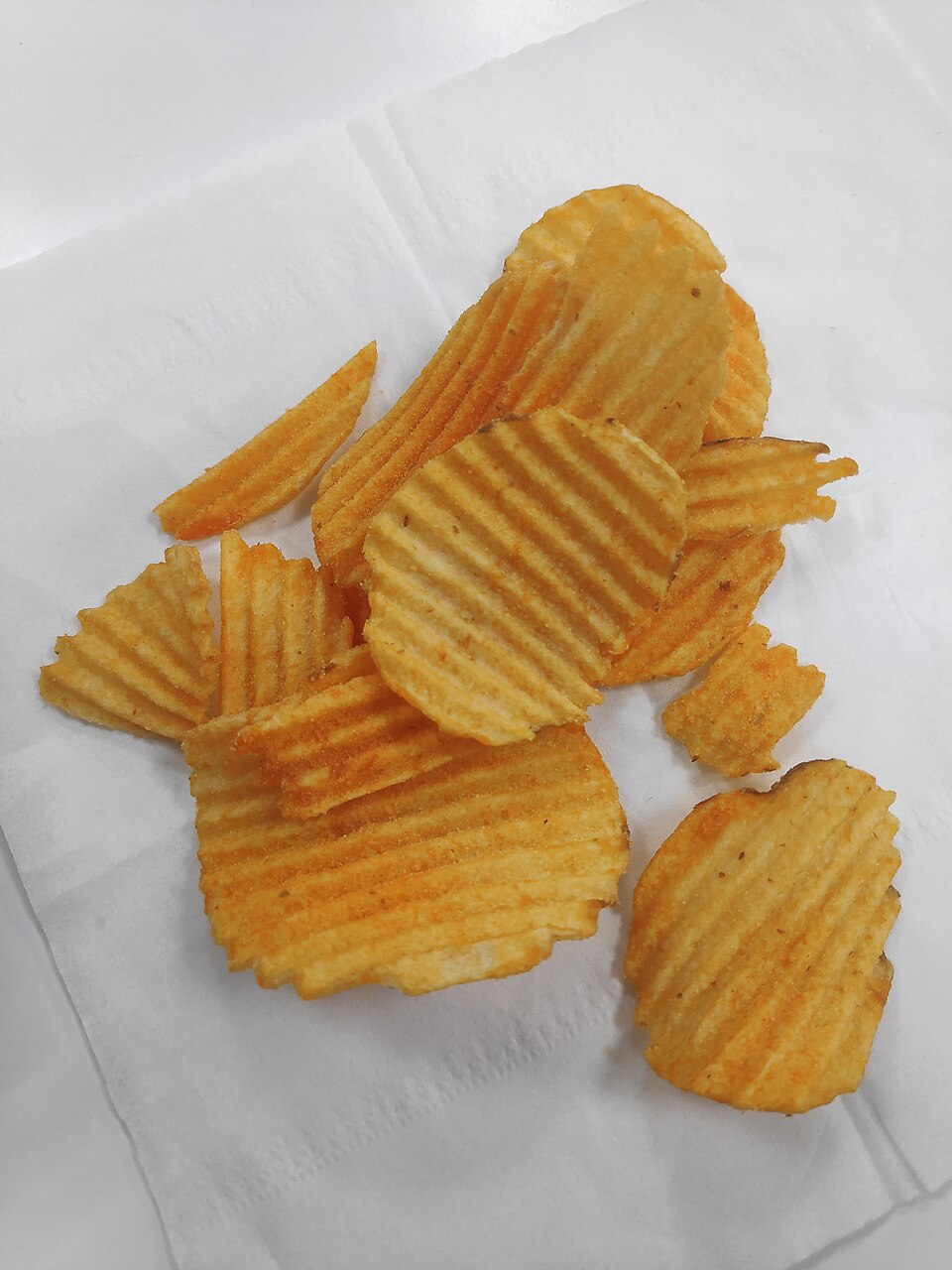 A handful of ridge-cut fried potato crisps spread on a white paper napkin
