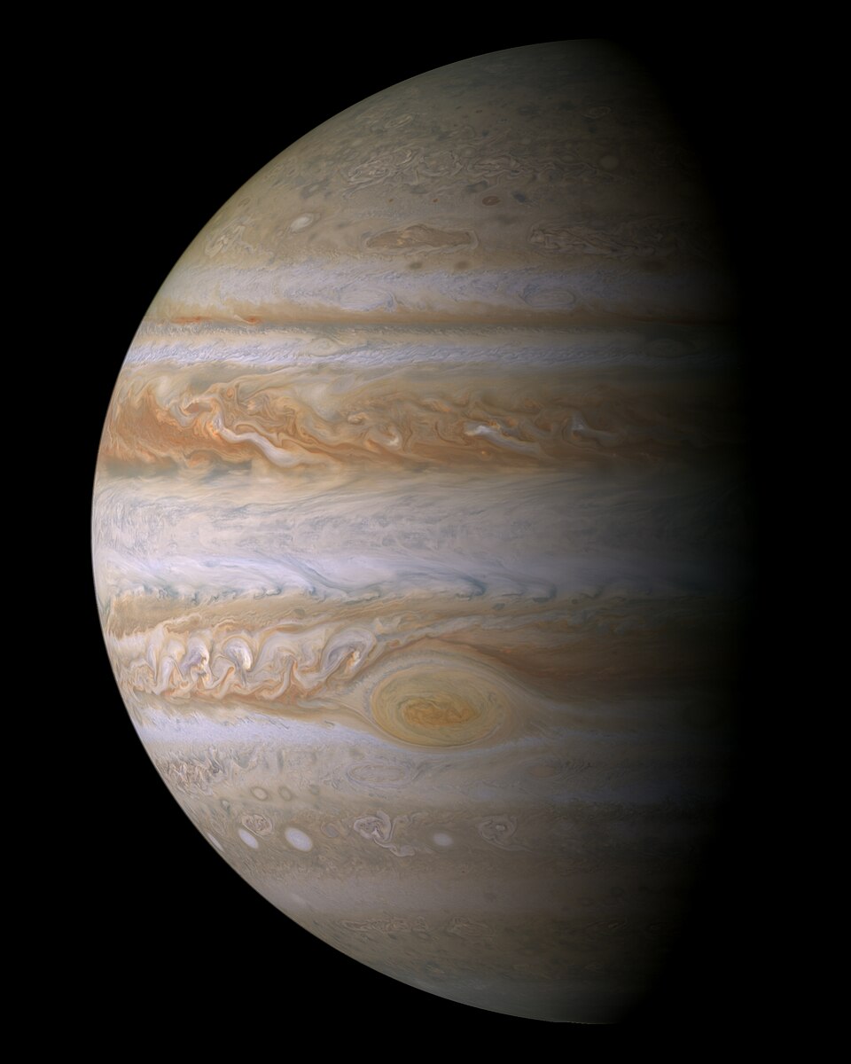 Jupiter photographed from the Cassini spacecraft, its banded cloud belts and the Great Red Spot lit from one side with the opposite limb in shadow