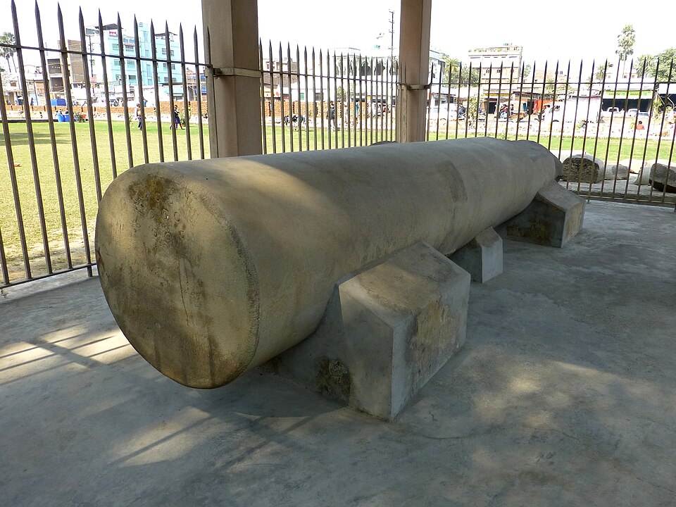 A single polished sandstone pillar shaft from the Mauryan eighty-pillared hall at Kumhrar, laid horizontally on concrete supports inside a railed shelter