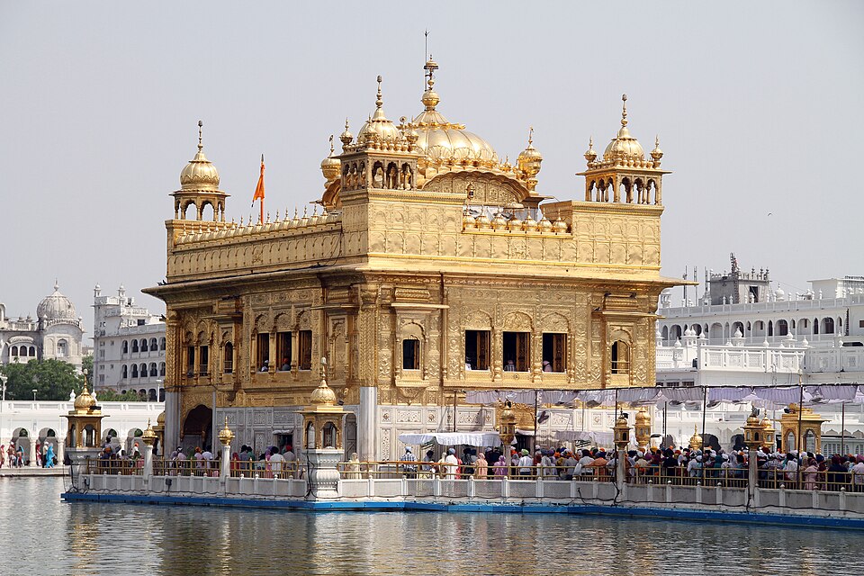 The gilded Harmandir Sahib rising from the sarovar at Amritsar, its gold-plated upper storey and dome above marble lower walls, pilgrims gathered on the surrounding walkway