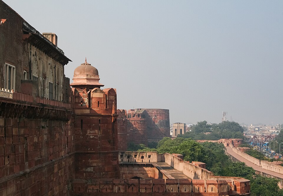 The red sandstone ramparts of Agra Fort curving away above a lower outer wall, a domed chhatri standing on a projecting bastion