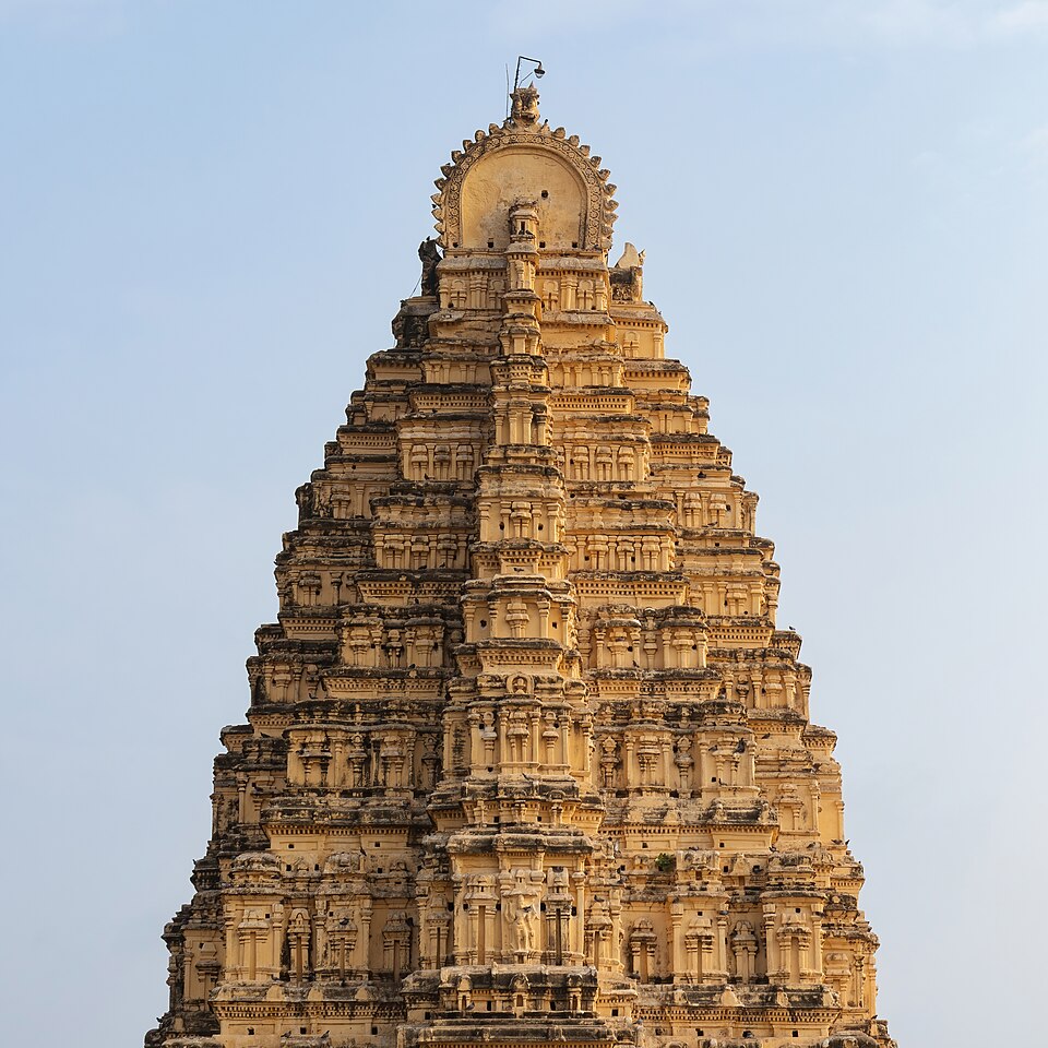 The tiered gopuram of the Virupaksha temple at Hampi rising against a clear sky, each storey crowded with carved figures and miniature shrines