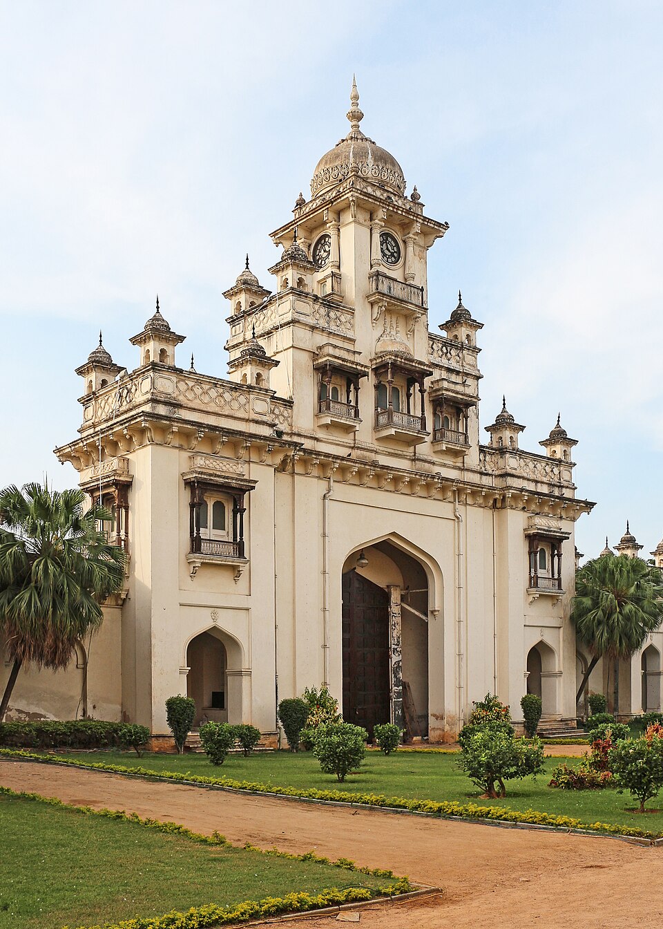The clock-tower gateway of Chowmahalla Palace in Hyderabad, a pale stuccoed facade with a high arched entrance, jharokha balconies and small domed turrets along the roofline