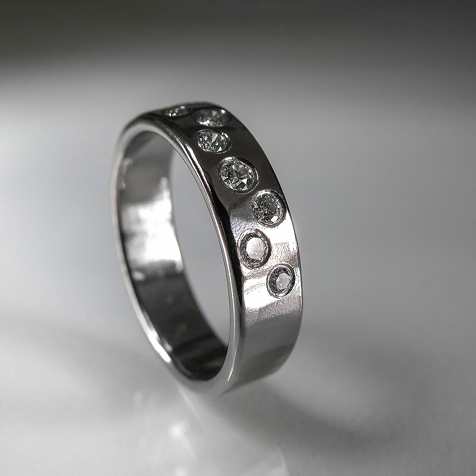 A polished silvery-white gold band ring set flush with small brilliant-cut diamonds