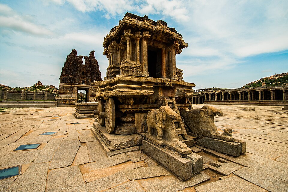 The carved stone chariot in the Vitthala temple courtyard at Hampi, with two stone elephants in front and ruined temple towers behind