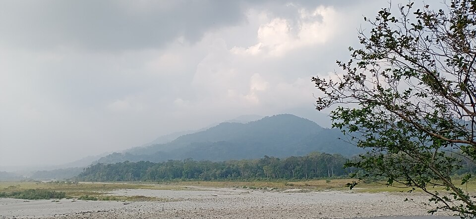 The wide braided gravel bed of the Manas River in Assam, with forested Bhutan foothills rising behind