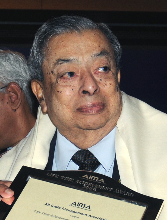 Verghese Kurien in later life, in a light jacket, holding a lifetime achievement award plaque