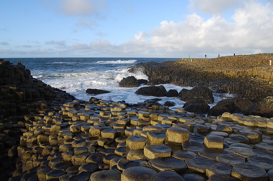 Interlocking hexagonal columns of basalt forming a rocky shore platform at the sea edge, the tops worn flat by waves