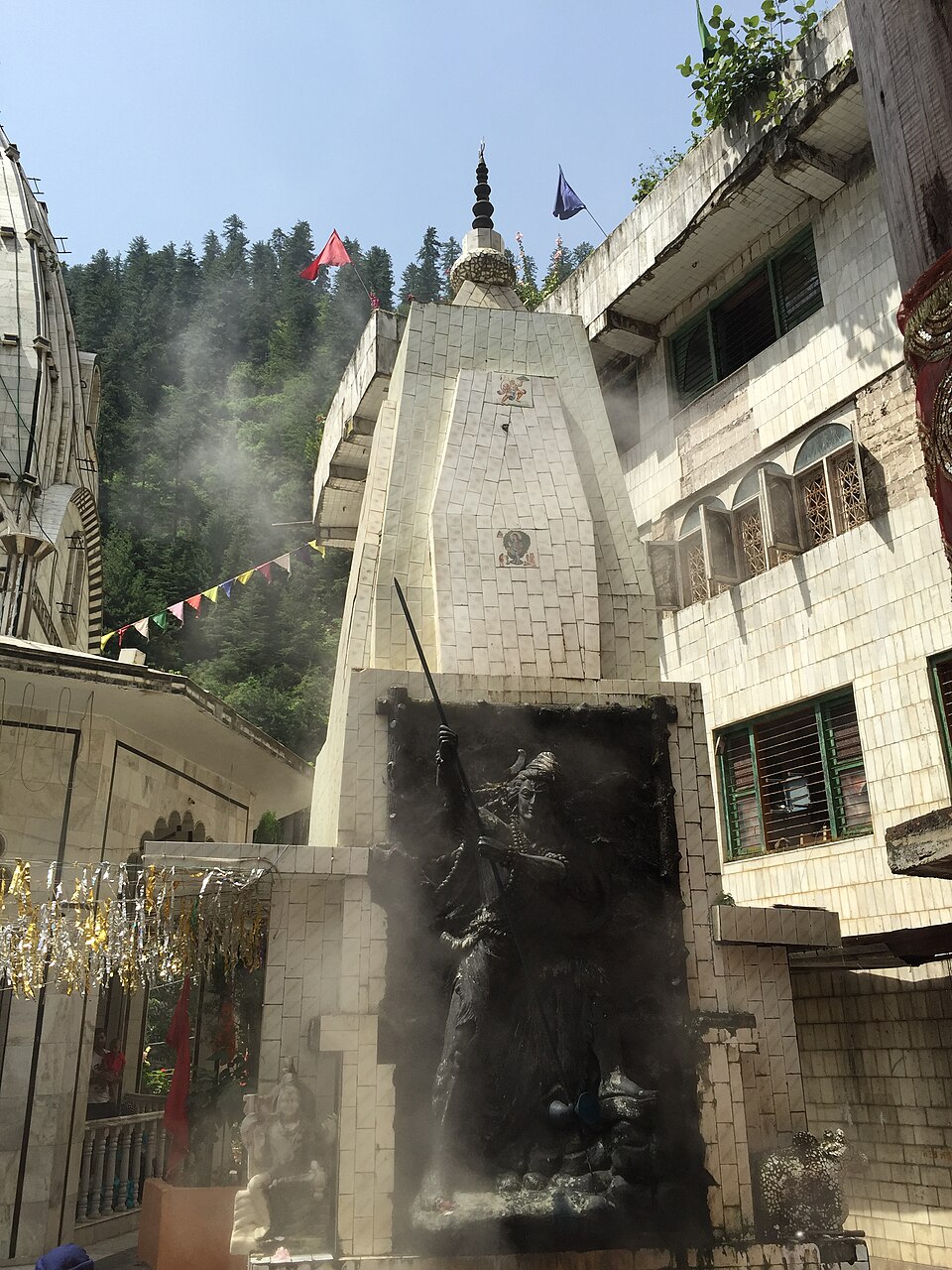 Steam drifting across the temple courtyard at Manikaran in the Parvati valley, with forested slopes rising behind