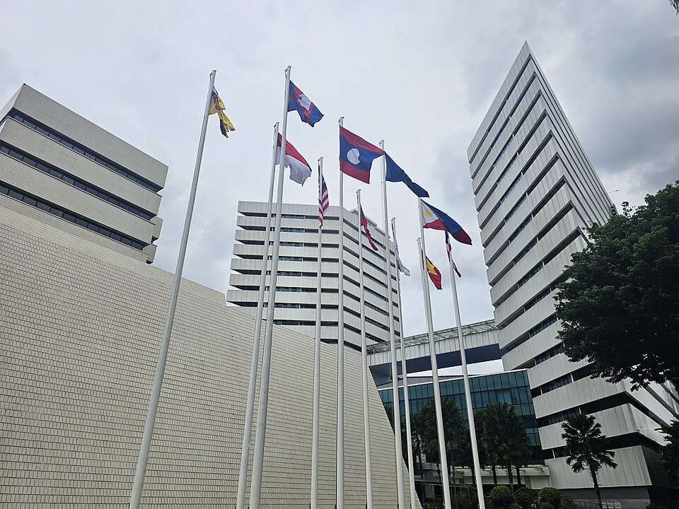 The ASEAN Secretariat complex in Jakarta seen from below, its office towers behind a row of flagpoles flying the member states flags