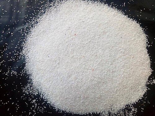 A heap of fine white quartz sand grains spread on a dark surface