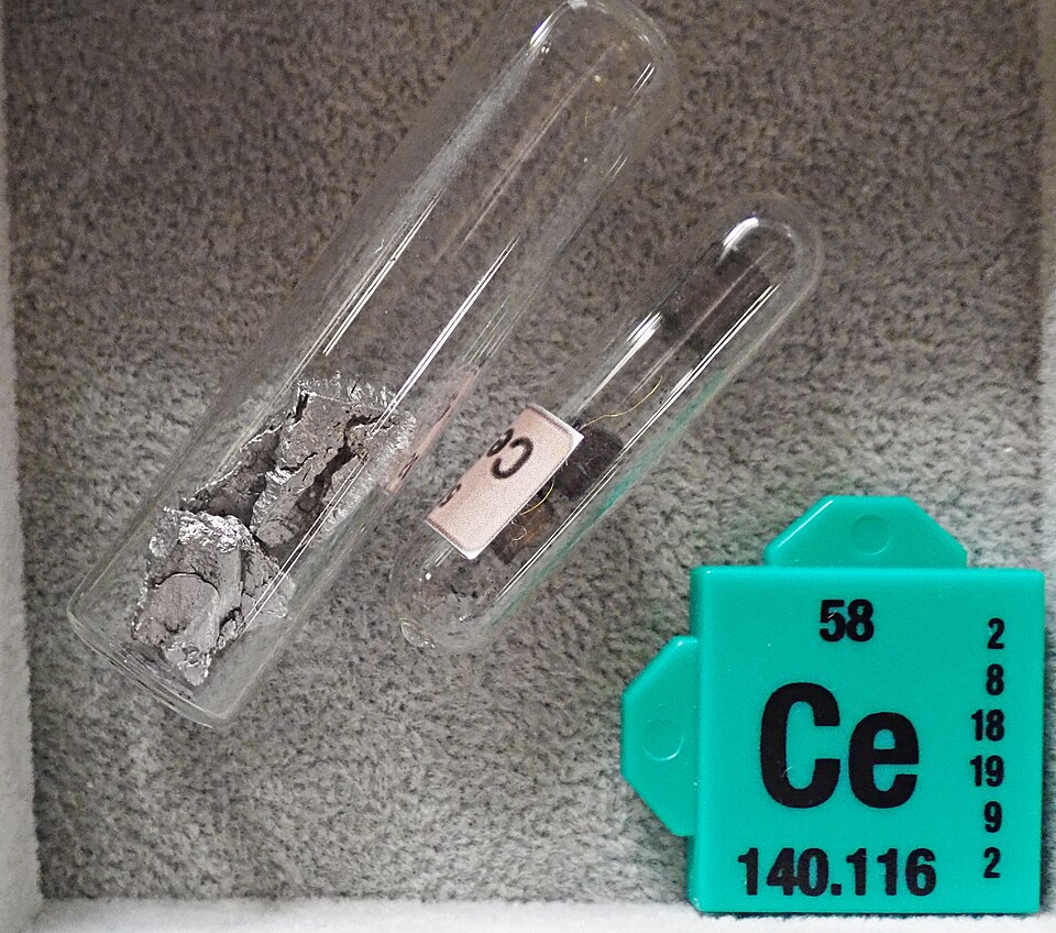 Two sealed glass ampoules holding pieces of grey cerium metal, beside a green element card reading Ce, 58, 140.116
