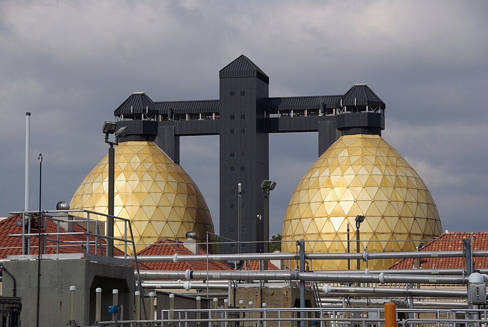 Two large egg-shaped anaerobic digester tanks with faceted golden shells, rising above the pipework of a treatment plant